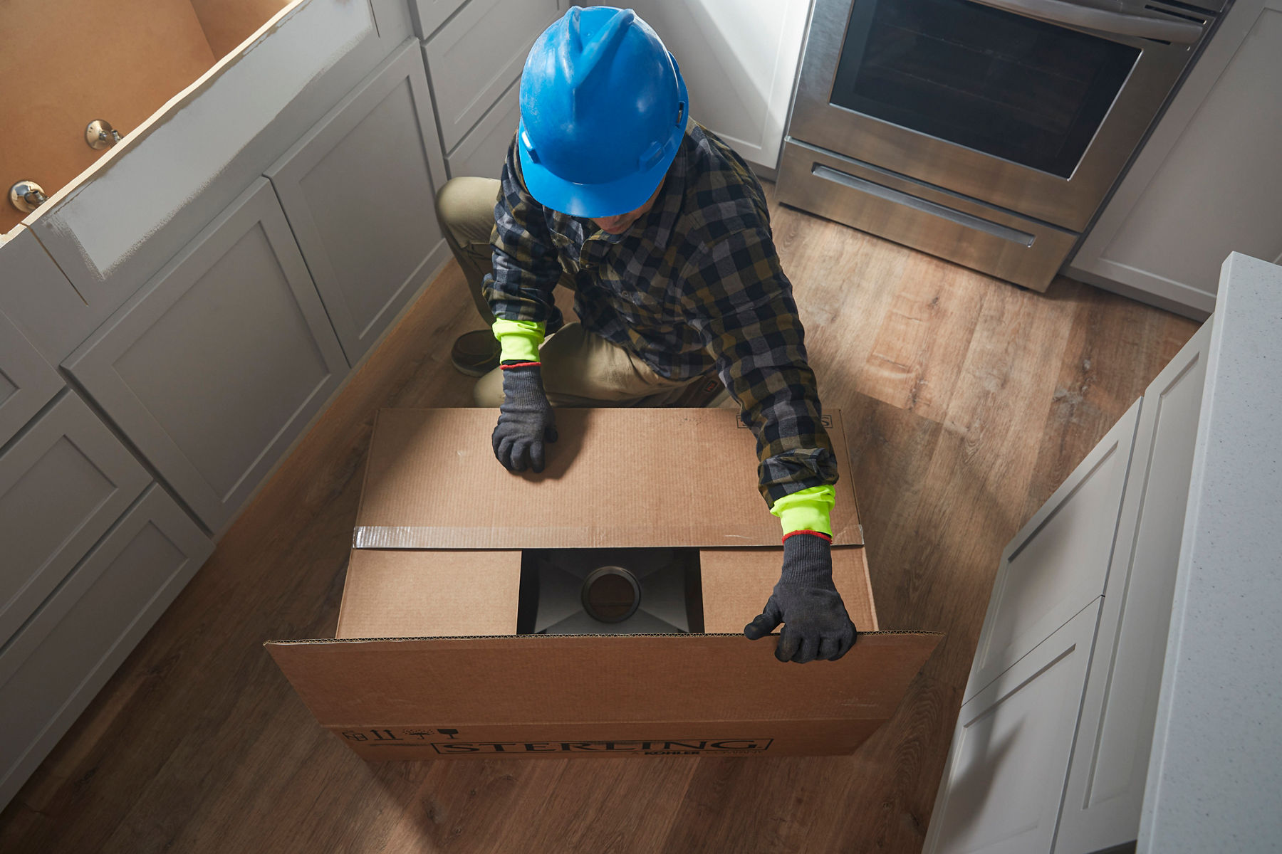 A contractor opens up a large cardboard box containing a Sterling stainless steel kitchen sink.