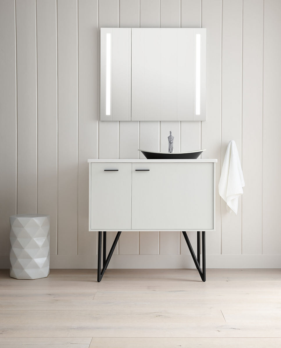 Une armoire à pharmacie Verdera Lighted de KOHLER est suspendue au-dessus d’un meuble-lavabo blanc aux pieds en métal et d’un lavabo en surface foncé.