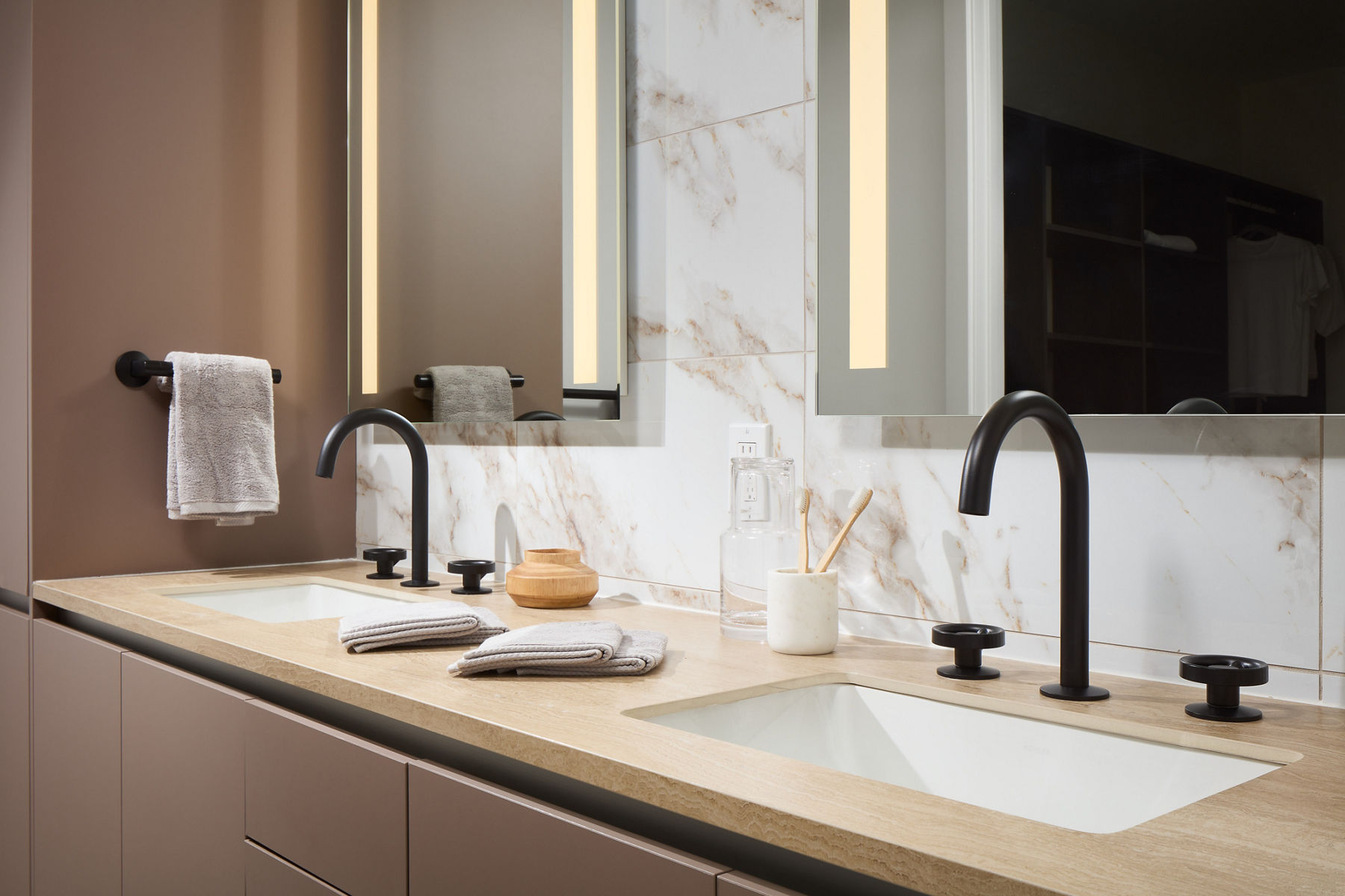 Photo of bathroom sink area with double sink and luminated vanities fitted with Kohler faucets and handles in matte black.