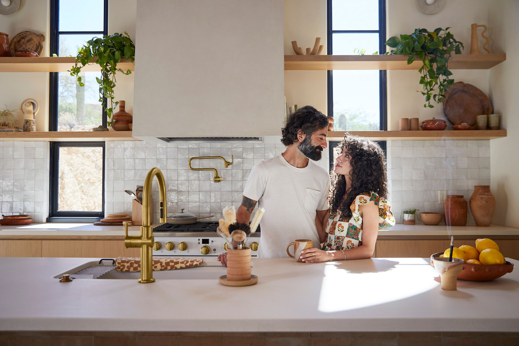 Portrait of Robert and Christina Martinez, the couple known online as New Darlings, standing in their kitchen close to each other and enjoying coffee together. They are looking at each other, standing behind the kitchen counter and sunlight from the large window behind them is creating a warm glow and shadows. 