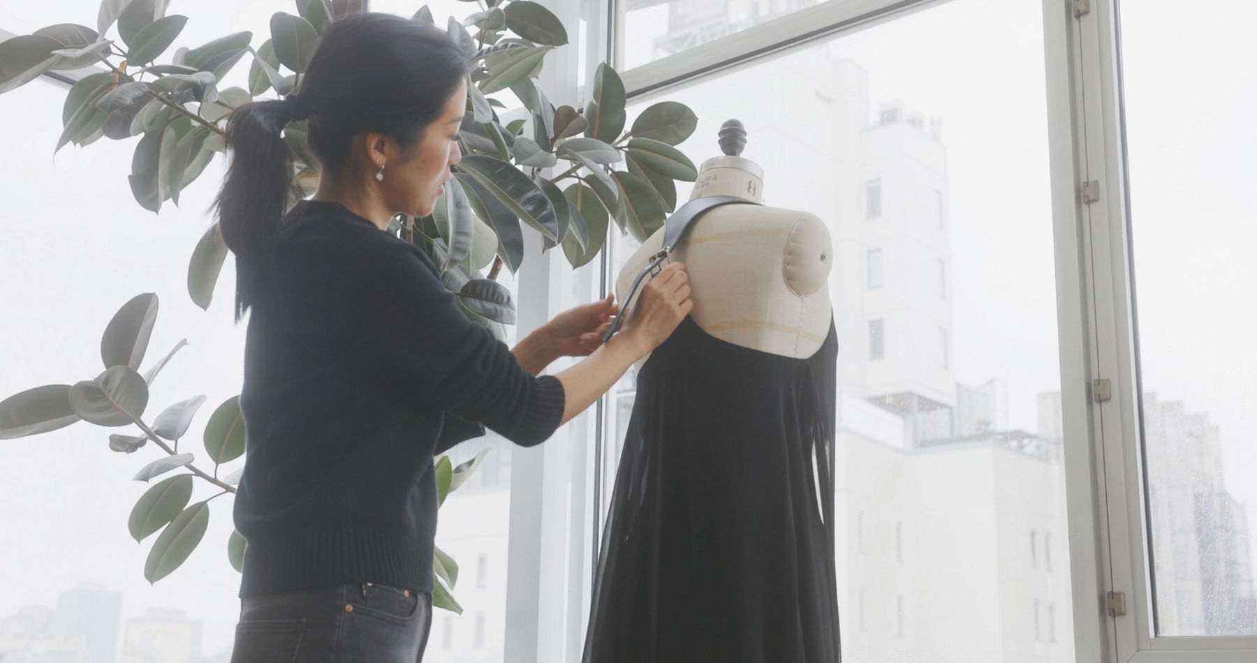 Creative director Laura Kim leans against a table full of fabric swatches and design tools in a studio space.