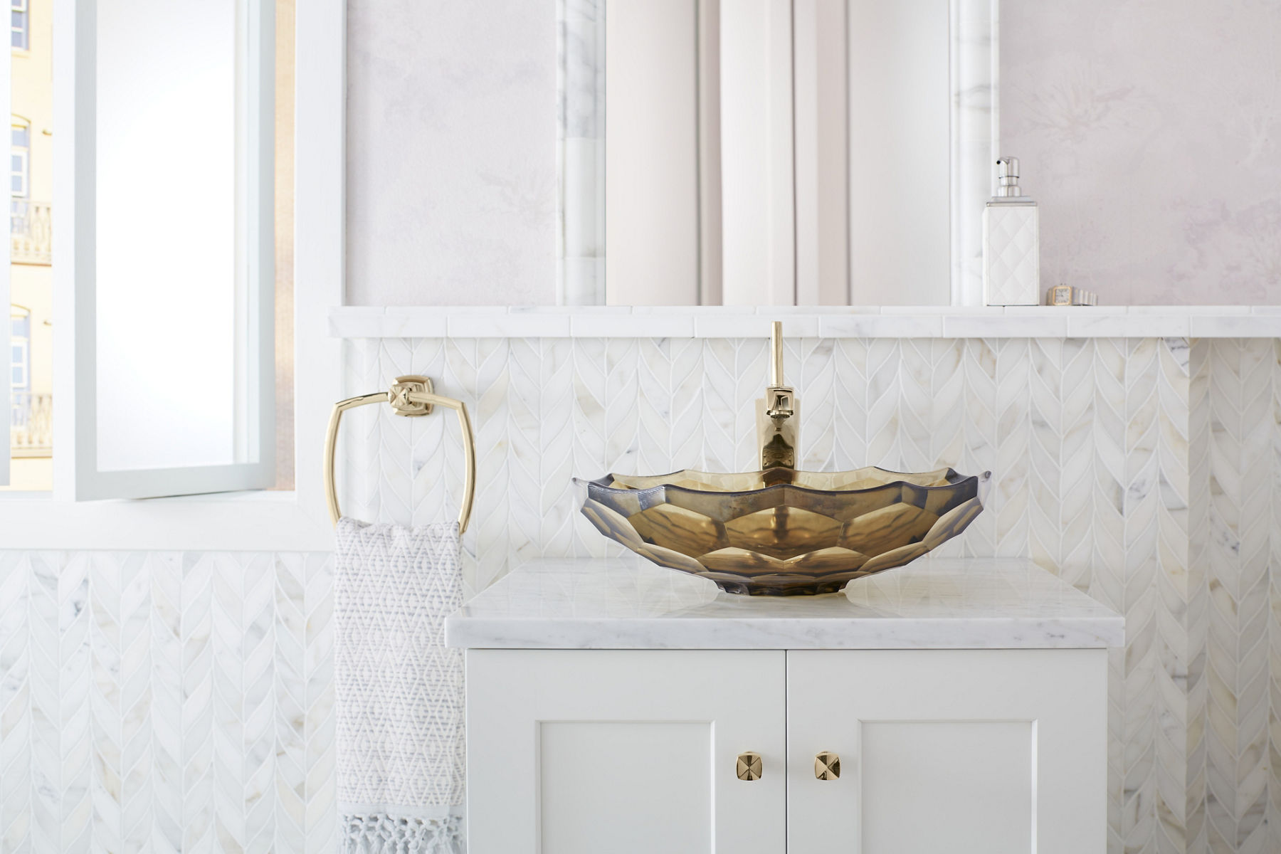 Lumière du jour dans une salle de bain aux tons blancs avec fenêtre ouverte donnant sur un paysage urbain avec un meuble-lavabo blanc avec quincaillerie d’armoire doré français Vibrant, lavabo en surface en verre Briolette et robinet Margaux.