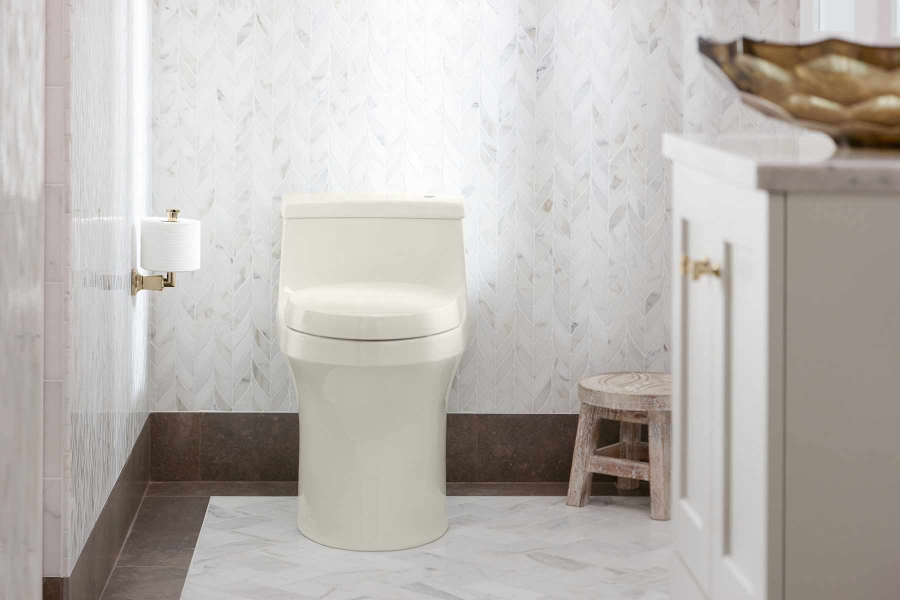 Une salle de bain avec des murs et un plancher en marbre, un meuble-lavabo blanc avec un lavabo en surface en verre à facettes et une toilette monopièce sans contact Comfort Height San Souci de KOHLER.