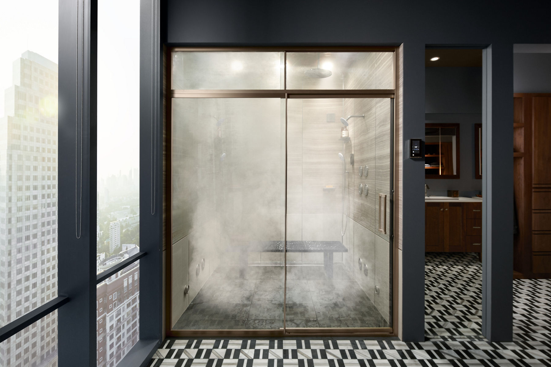 La vapeur remplit une douche à vapeur KOHLER avec des portes en verre et des garnitures en bronze dans une salle de bain gris foncé avec des fenêtres sur toute la longueur montrant la ligne d’horizon de la ville.