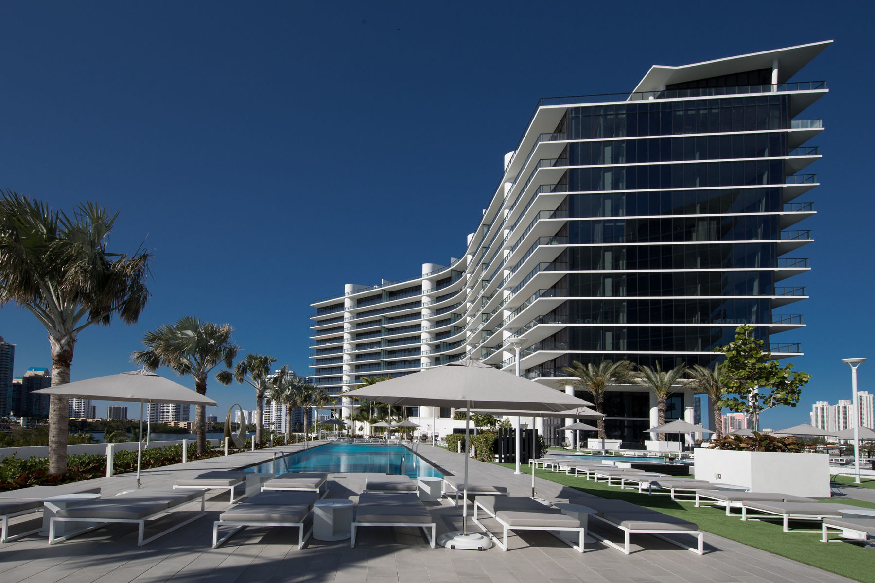 Exterior view of the modern architecture of Prive at Island Estates, featuring contrast between glass and white accents and the pool with lounge chairs and umbrellas.