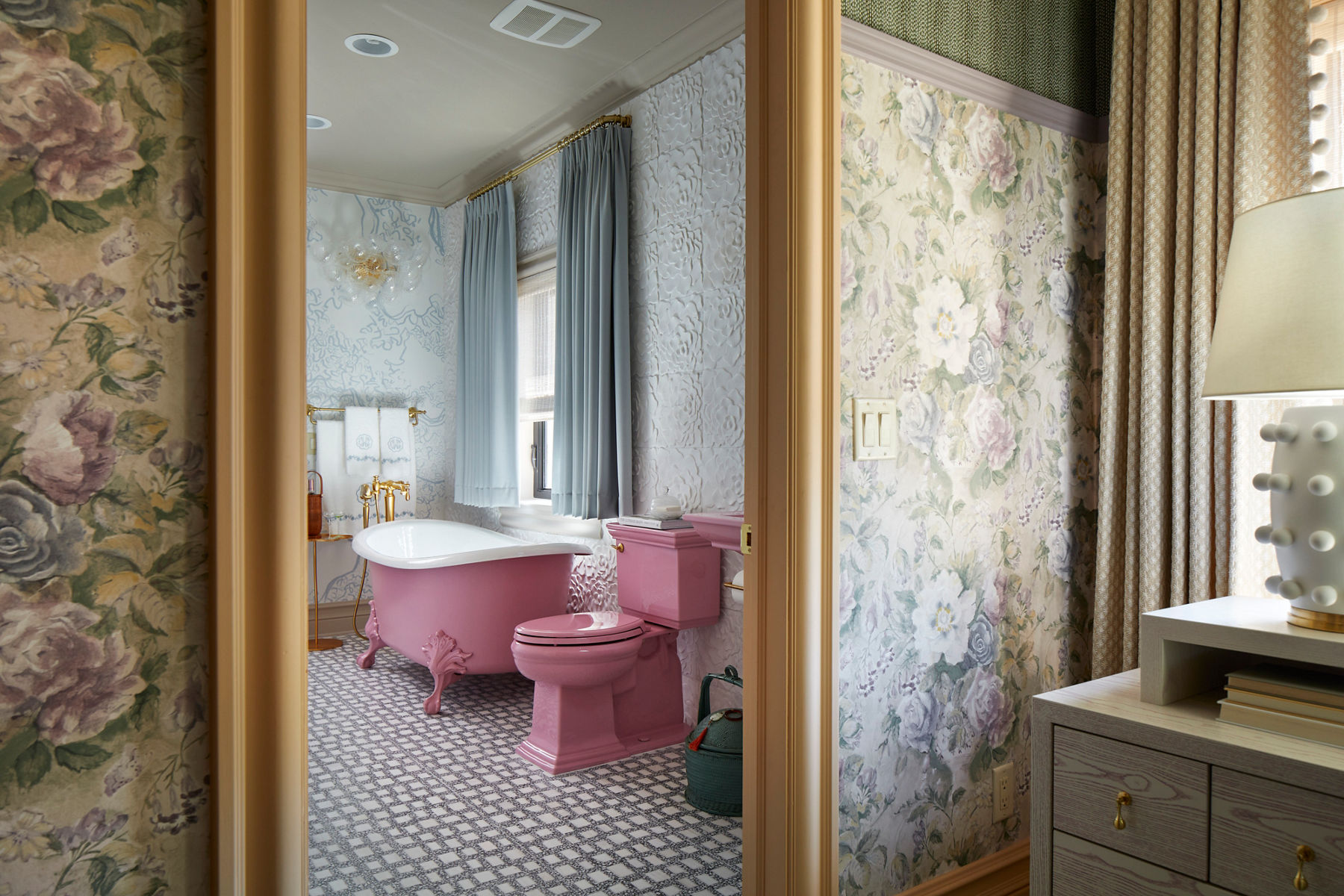 Through a bedroom doorway, looking into a bathroom with a matching pink toilet and claw-foot bath.