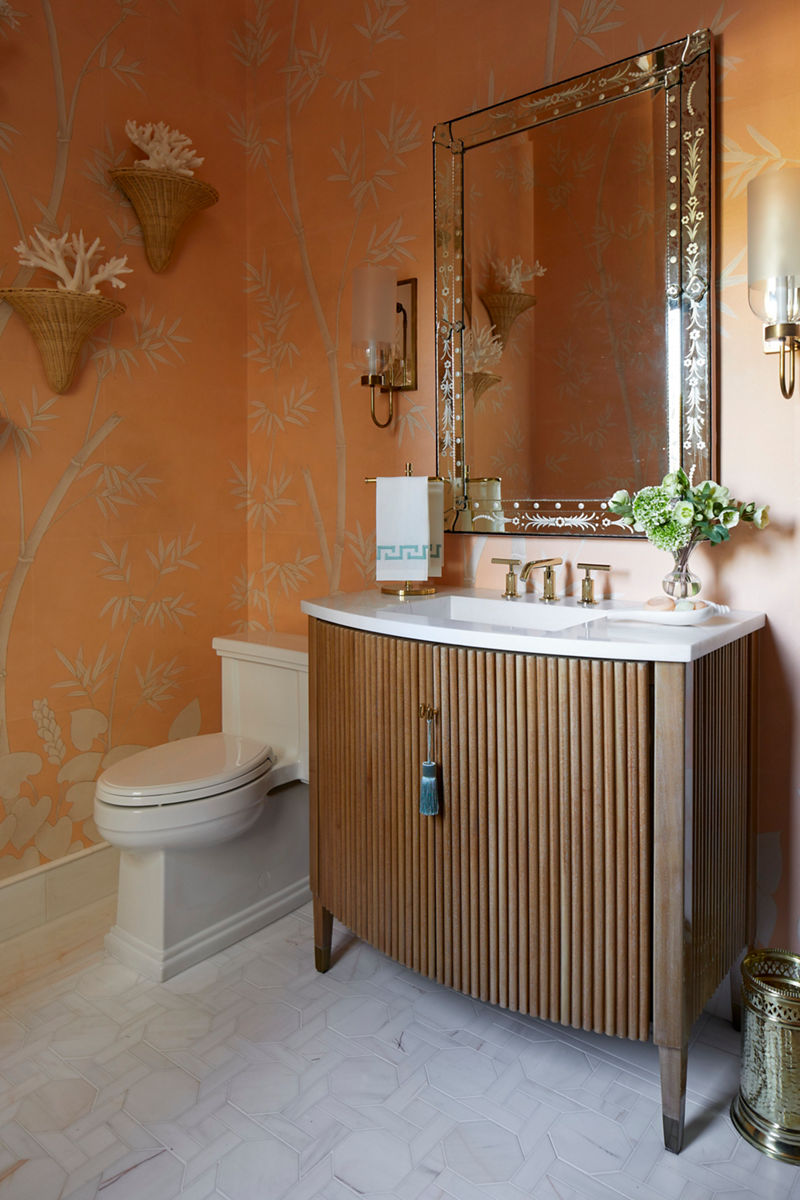Close-up image of a vanity and toilet in a powder room bathroom. The vanity is wood with intricate channels designed into the front cabinets, while the white counter top and polished chrome faucet are clean and modern.