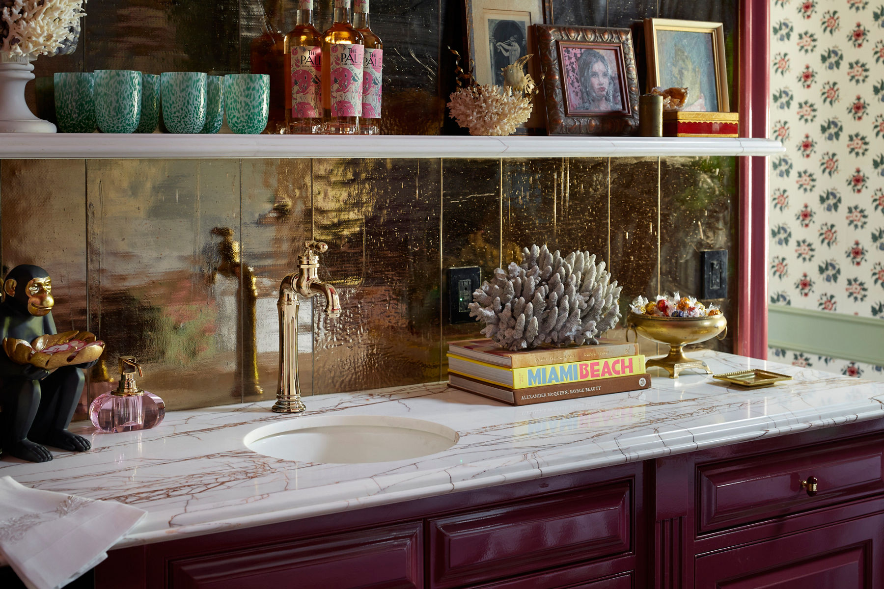 Image of a wet-bar space with books, glassware, picture frames and other decorations around the bar sink and faucet.