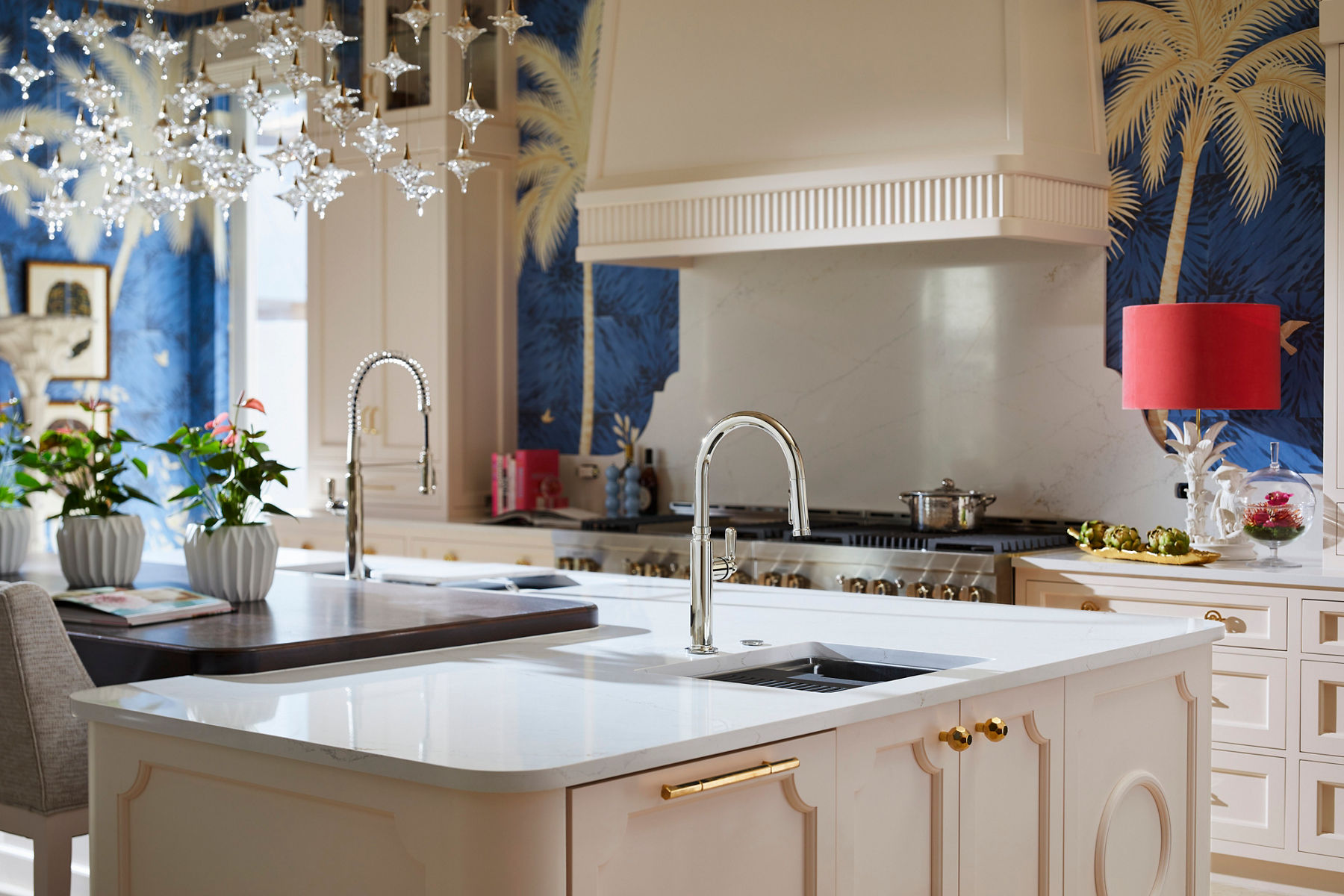 A kitchen in tones of white, peach, and blue with palm tree wall paper and a large island in the center.