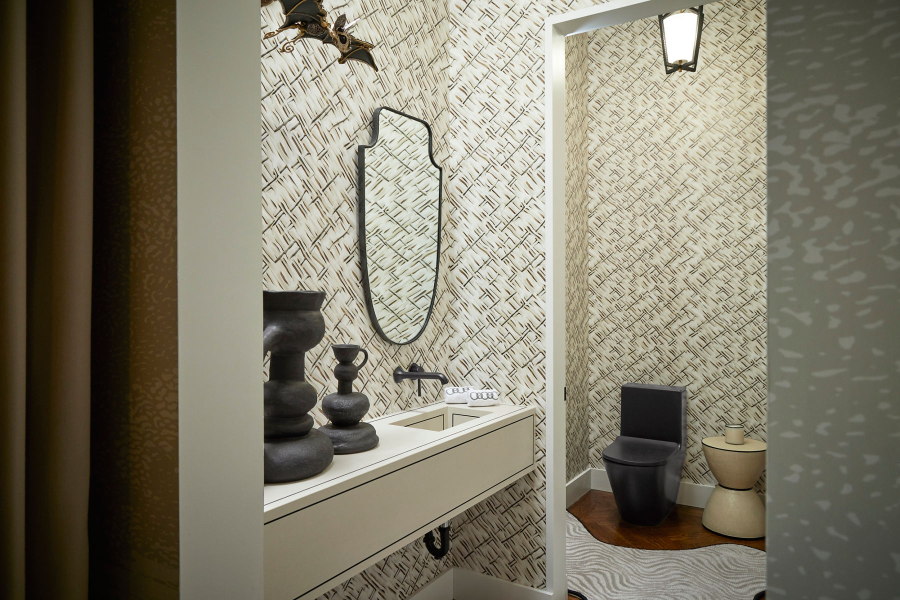 A black and white inspired room designed with a minimalist wallpaper throughout, black vase decor, a white undermount sink with a black faucet, and a black toilet to the far right hand side with a side table next to it.