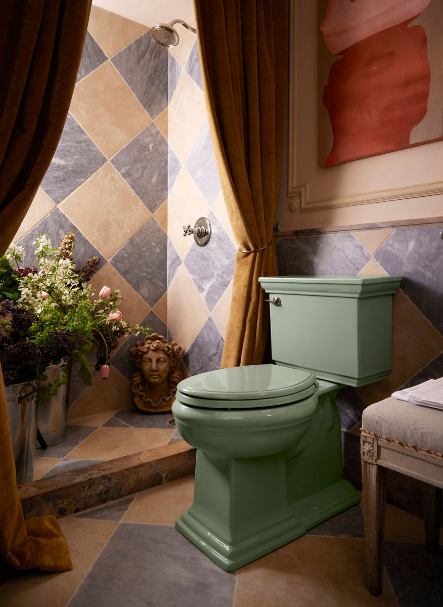 A close-up shot of a pale green toilet in a gray and brown tiled bathroom. There's flowers, a statue, a bench, and curtains around it.