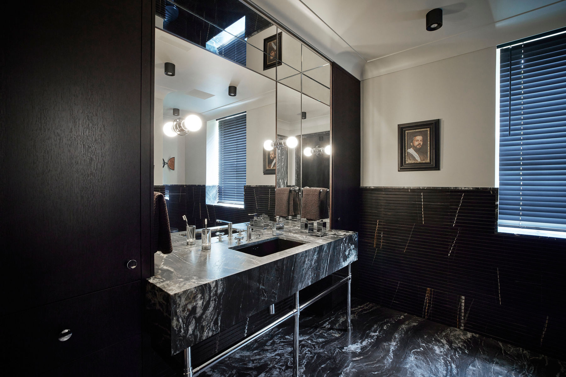 A glamorous bathroom and dressing room space designed with black marble, circular sconce lights, black window treatments, and a black marble vanity with a silver faucet.