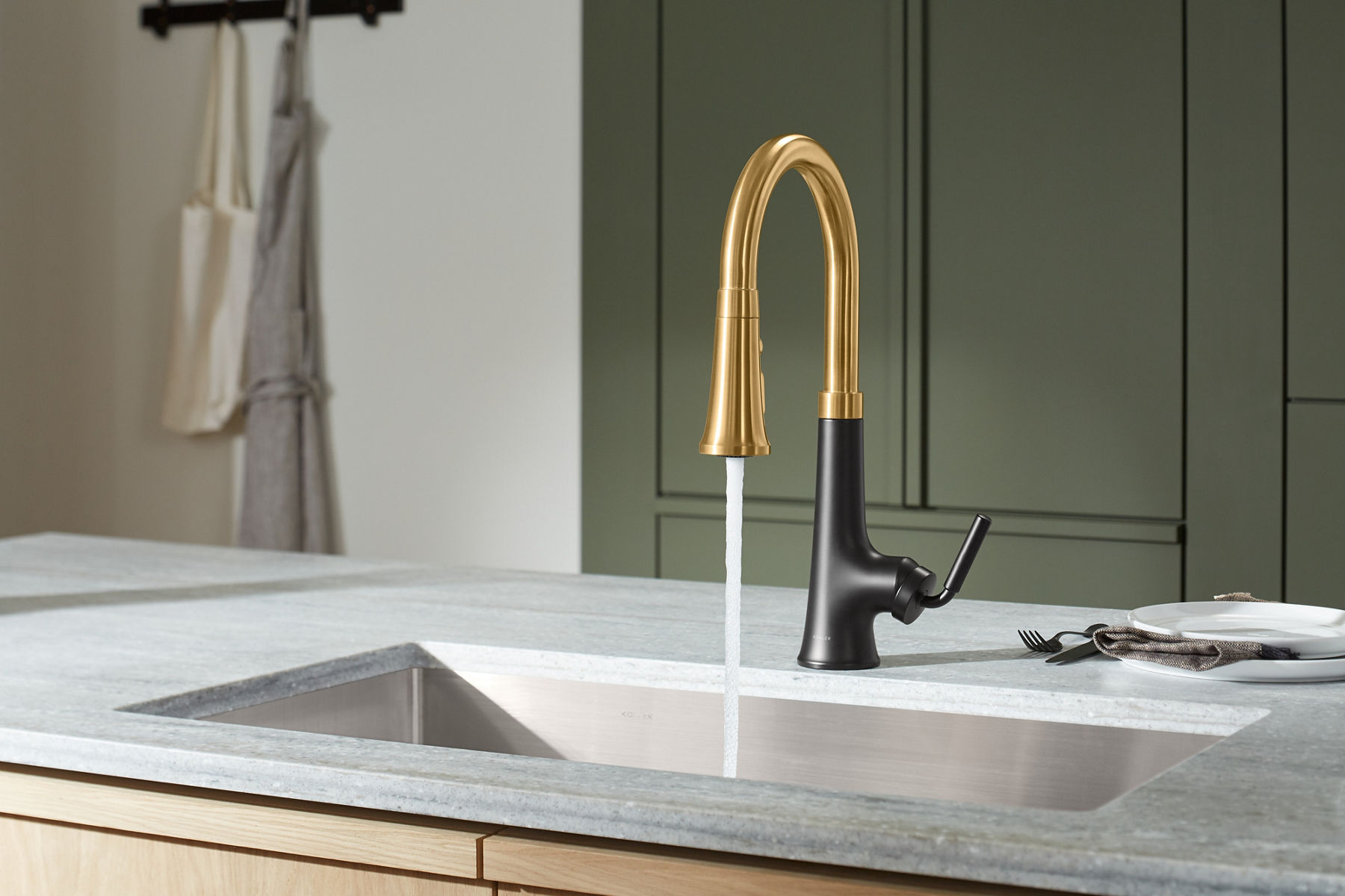 A two tone matte black and brushed moderne brass kitchen faucet on a white counter top with green walls.