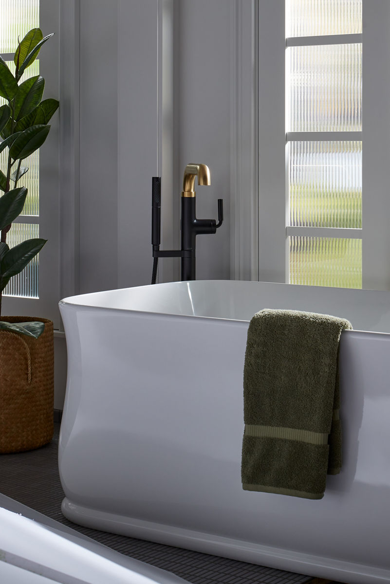 A green towel hangs on the side of a white KOHLER Imperator freestanding bath with Tone freestanding bath filler.