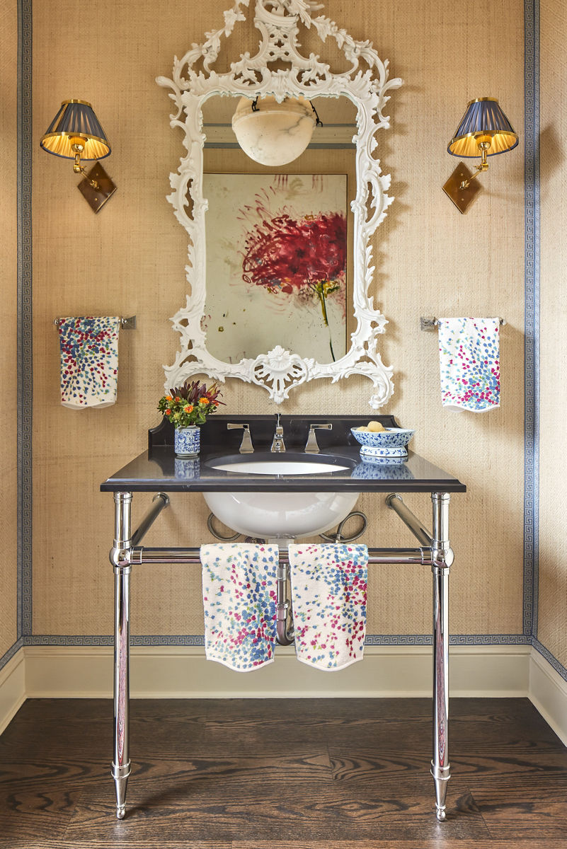 Un meuble-lavabo avec un lavabo de table console avec des pieds en chrome poli et un miroir orné avec un cadre blanc complexe contre un mur jaune doux.