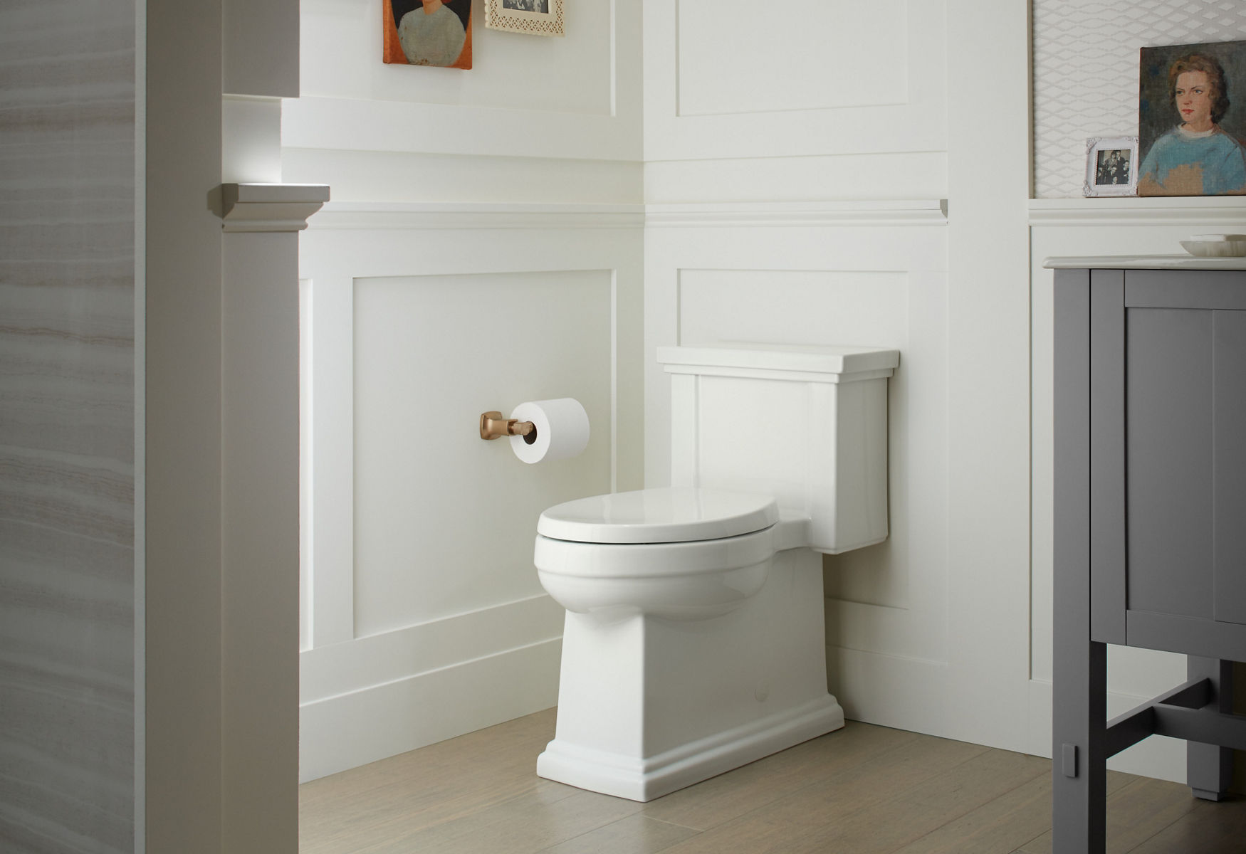 Une toilette allongée blanche Tresham de KOHLER dans une salle de bain avec un tableau blanc et des murs en latte.