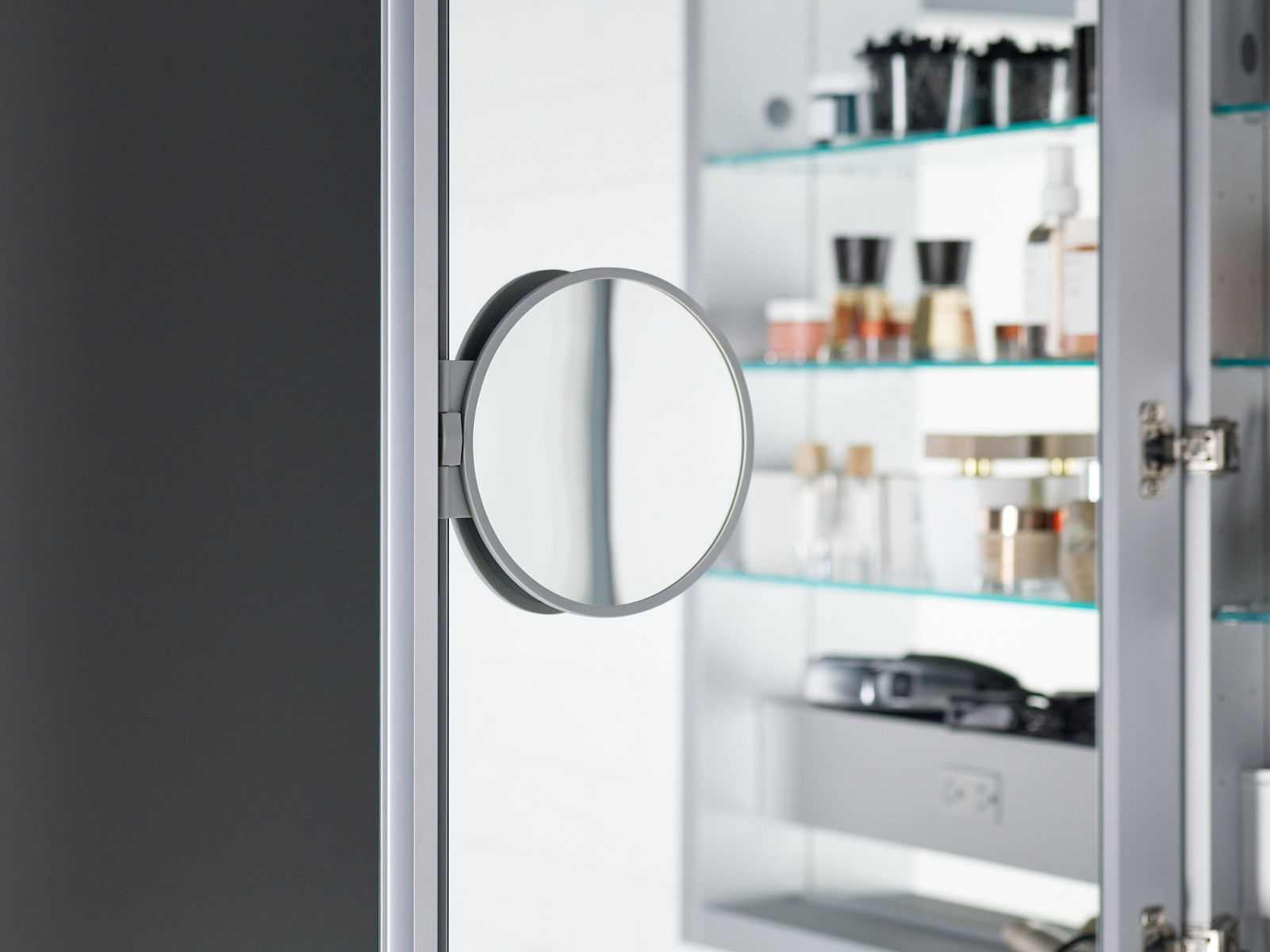Close-up detail of a fold-out magnification mirror connected to the interior door of a medicine cabinet.