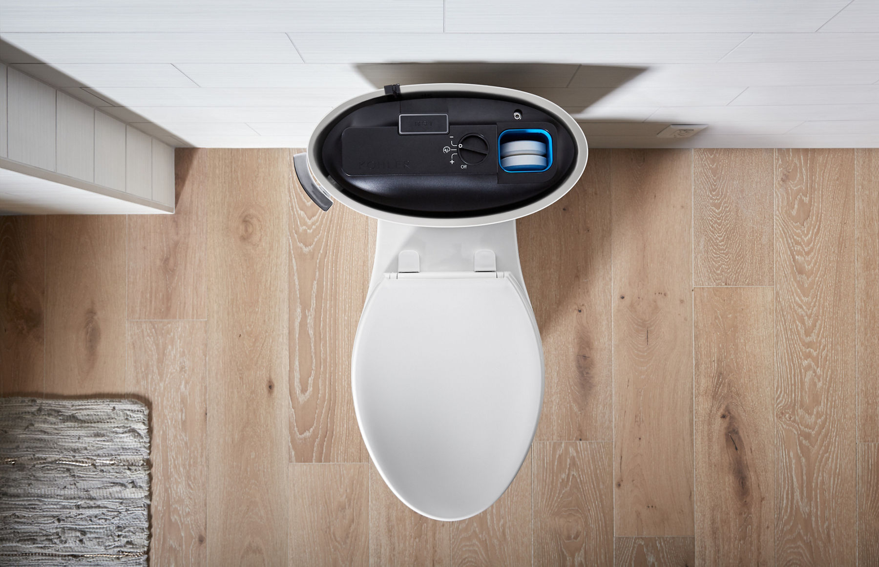 Top view of an open smart toilet tank, revealing internal components, including a water filtration system and control mechanisms, placed on light wood flooring.