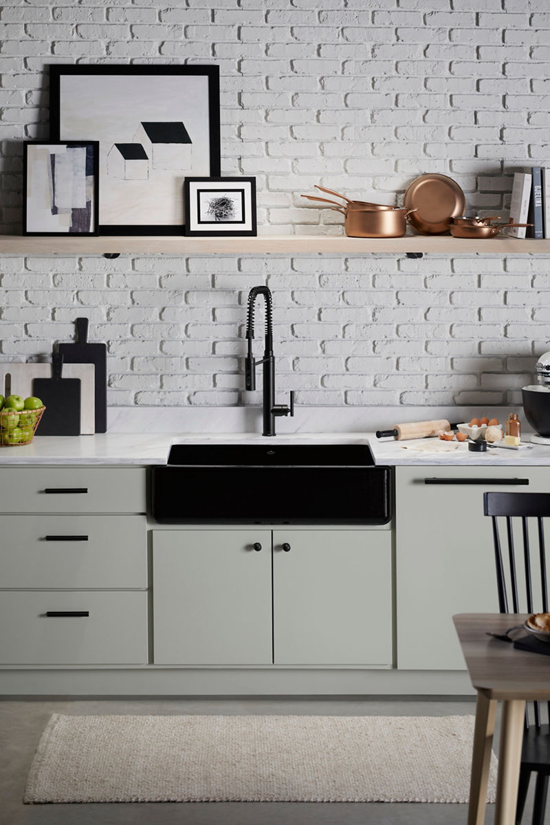 Modern kitchen with a black farmhouse sink, matte black spring-spout faucet, and white brick backsplash, complemented by open shelving with decor and cookware.