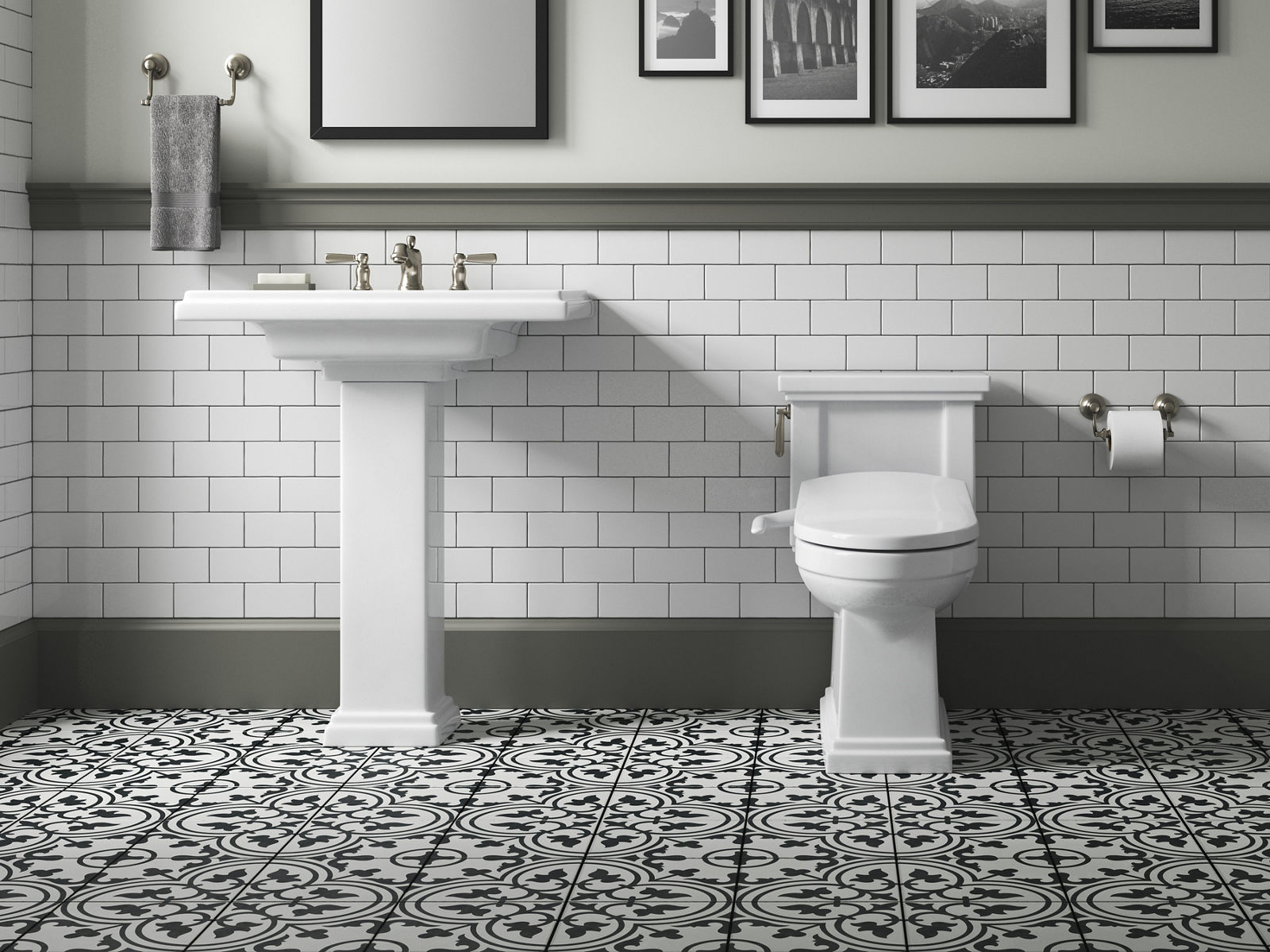 Un lavabo sur colonne blanc Tresham de KOHLER dans une salle de bain avec murs en carreaux de métro blancs, bordures grises et carreaux de plancher à motifs noirs et blancs.