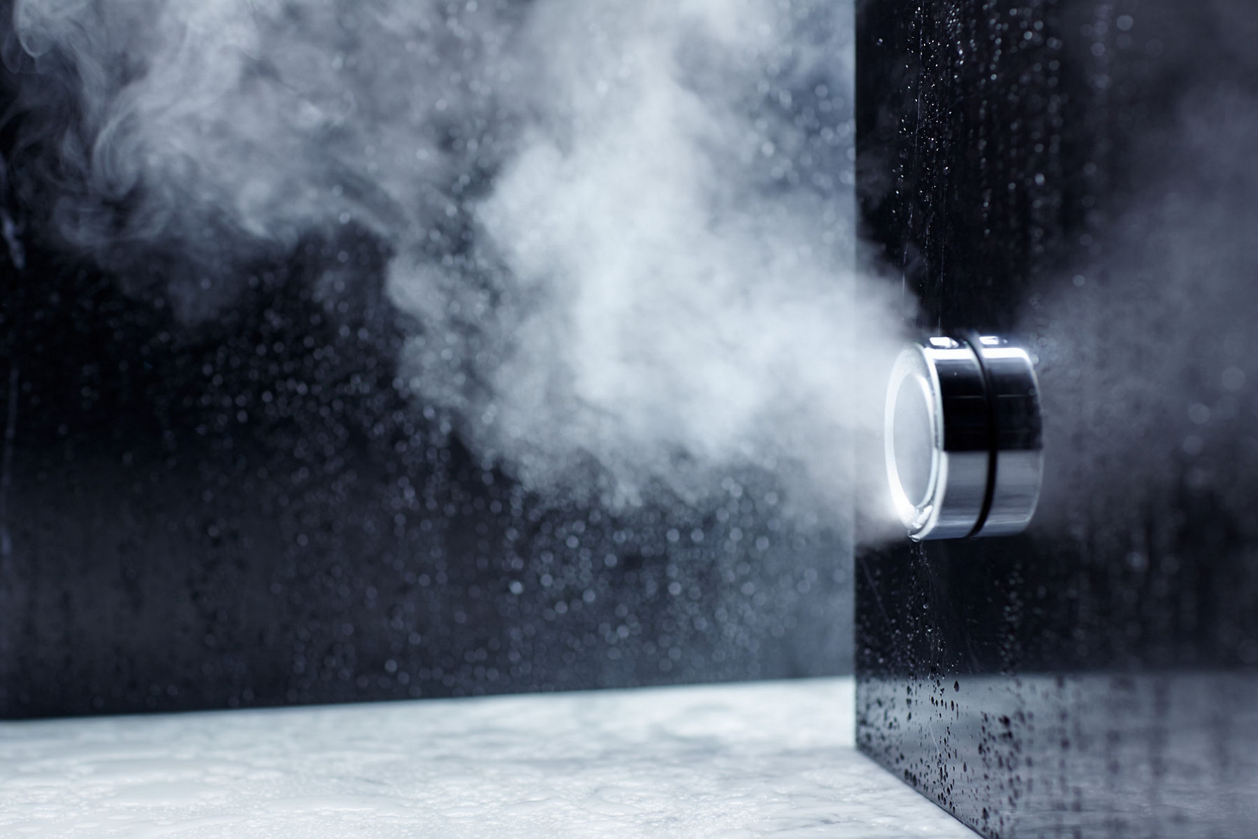 Vapeur sortant d’un robinet de vapeur KOHLER en chrome poli installé sur un mur de douche noir.