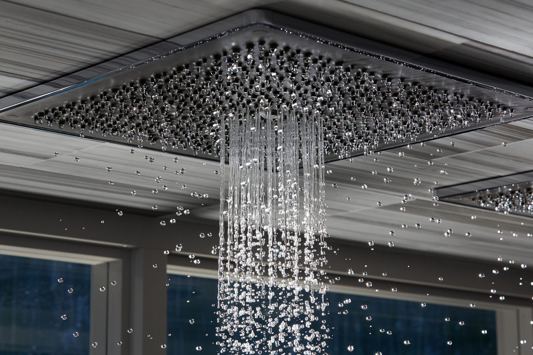 Gros plan de l’eau s’écoulant d’une pomme de douche à effet de pluie KOHLER montée au plafond d’une douche.