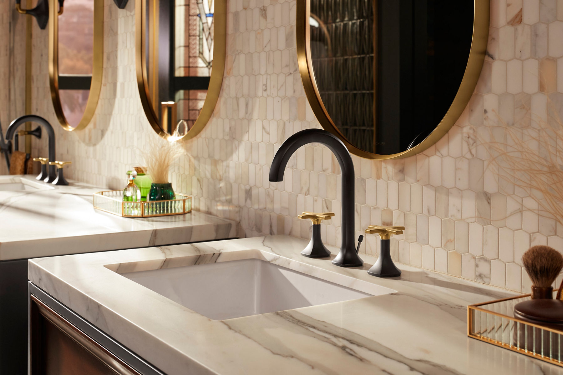 Un espace meuble-lavabo de salle de bain avec un comptoir en pierre et un mur de carreaux de couleur crème clair, ainsi qu’un robinet bicolore en noir mat et laiton brossé.