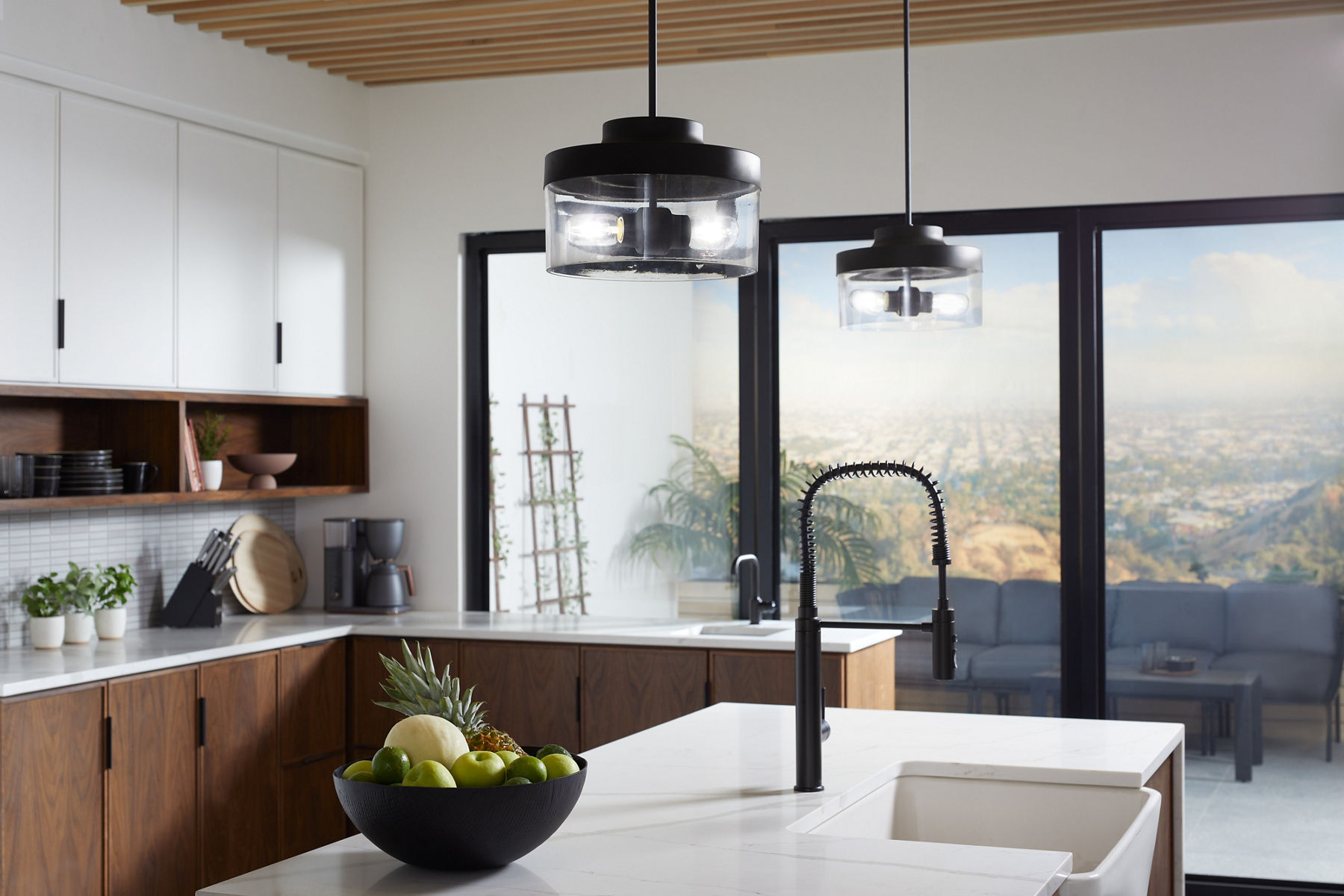 Two KOHLER pendants with clear glass shades hang from a wood paneled ceiling.