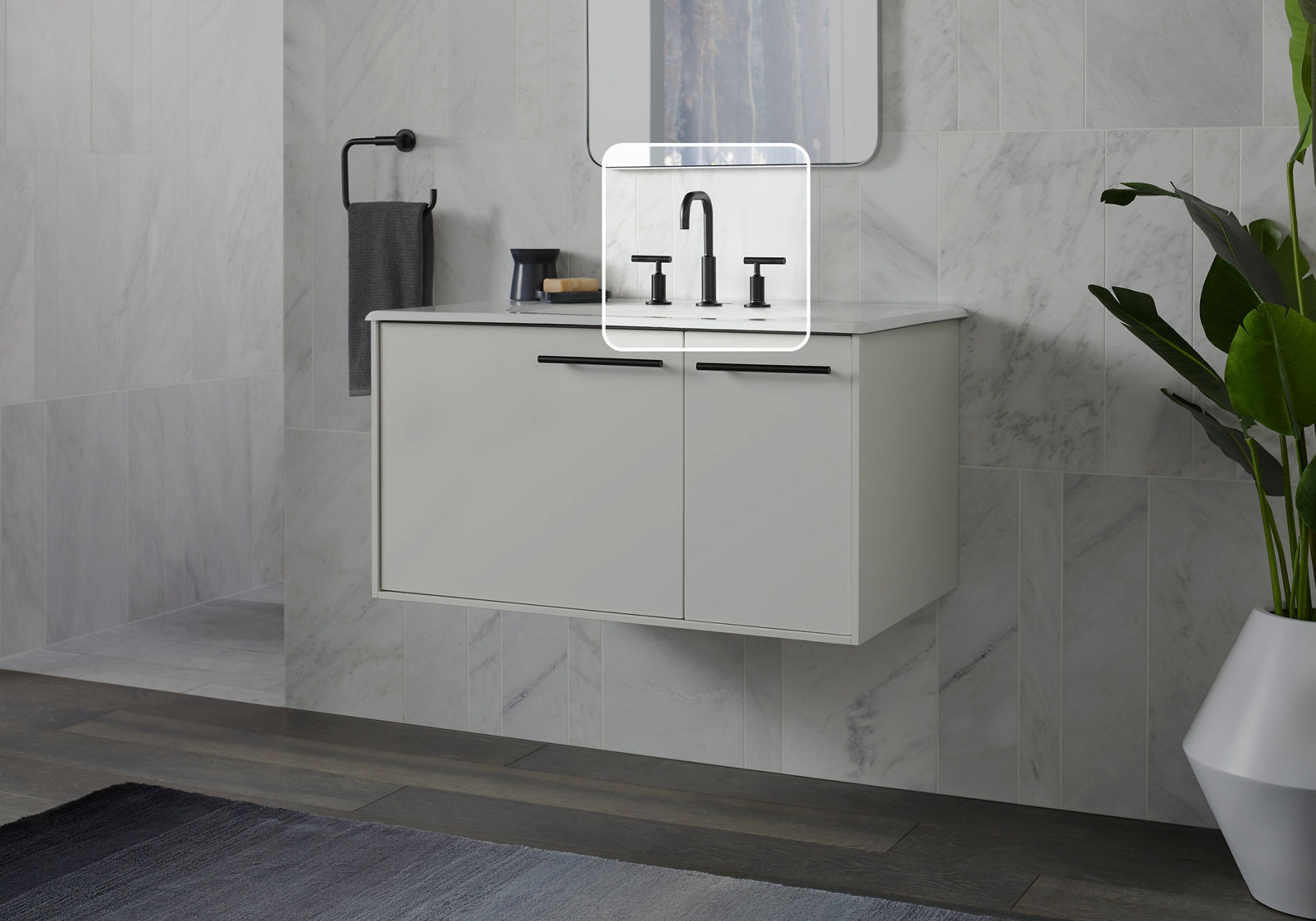Un meuble-lavabo de salle de bain dans des tons de gris et de noir mat avec le robinet mis en valeur par un carré blanc graphique placé autour et un effet assombrissant appliqué à l’extérieur du carré.