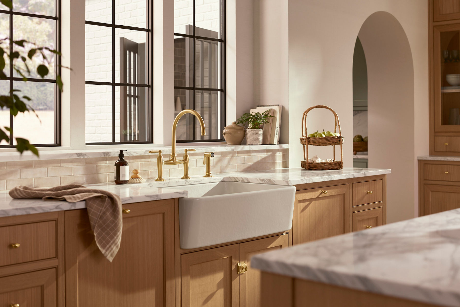 A bathroom vanity top with a Kohler Casita bathroom faucet with a gold finish and lever handles with other vanity accessories in the background