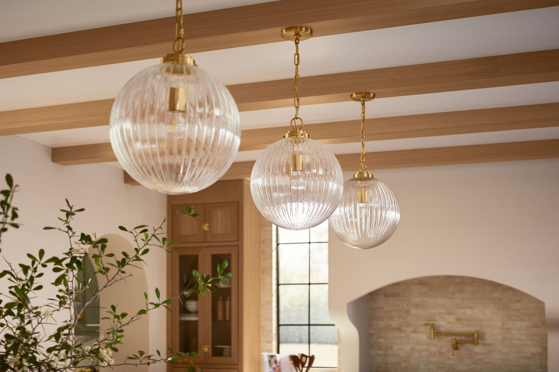 Three pendent lights installed above a kitchen counter in vibrant modern brass finish
