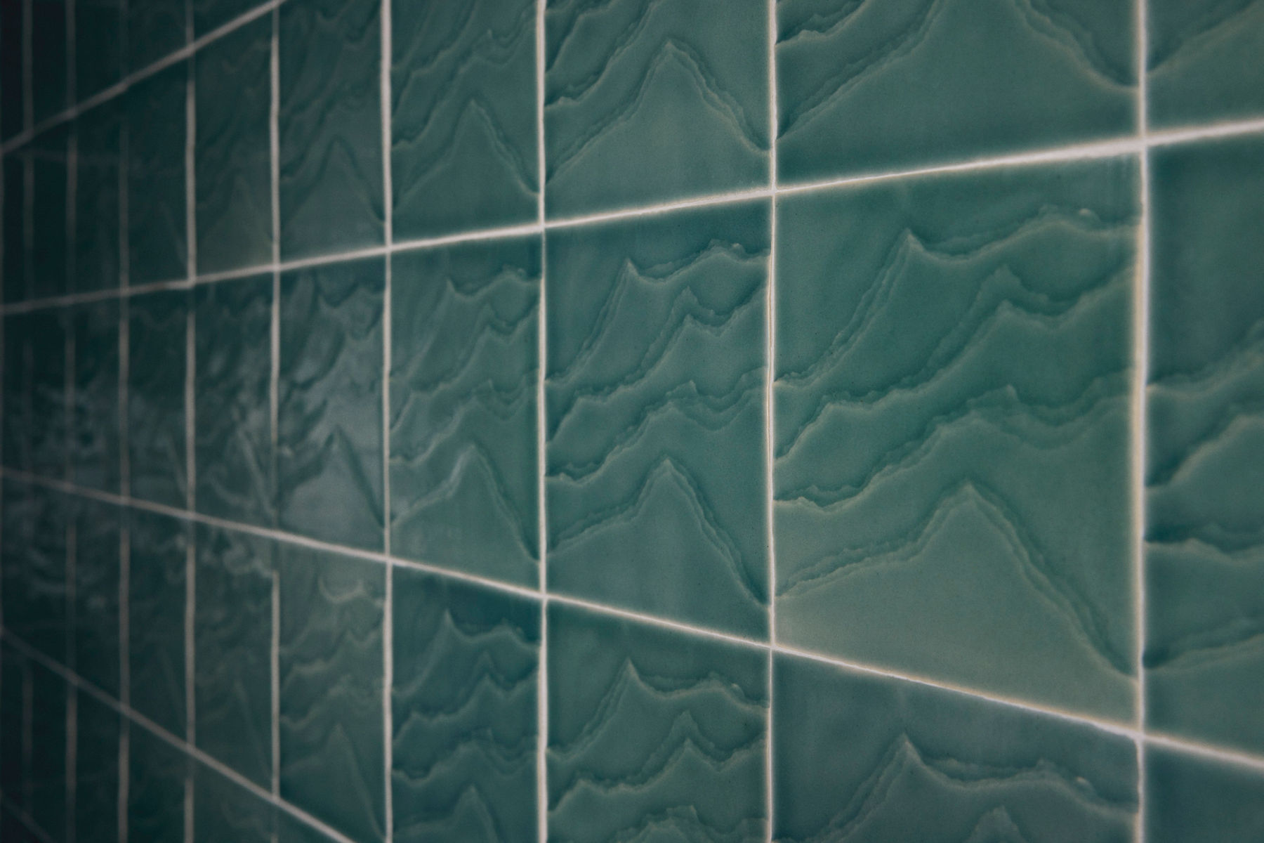 A close-up image of green ceramic tiles with a wavy, textured pattern that resembles natural stone formations.