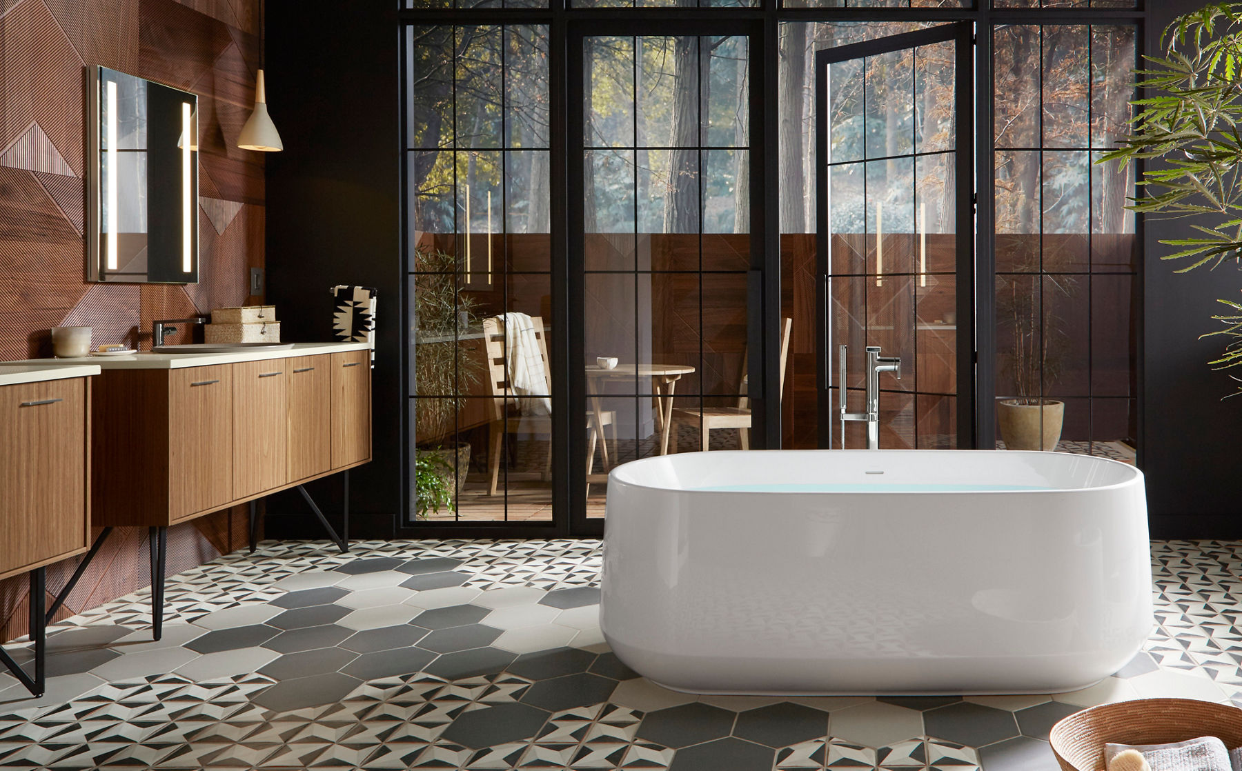 Une baignoire blanche Ceric de KOHLER au milieu d’une salle de bain avec un mur à panneaux de bois, deux meubles-lavabos muraux Jute, un plancher en carrelage à motifs et des fenêtres allant du plancher au plafond surplombant un balcon.