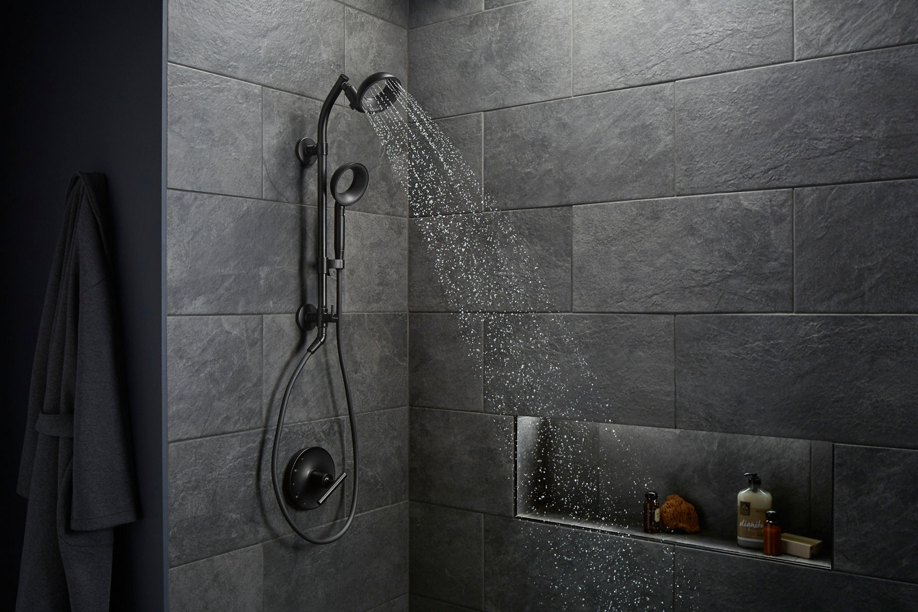 A shower with dark gray large-scale tile walls with a showerhead and handshower in matte black with hollow centers.