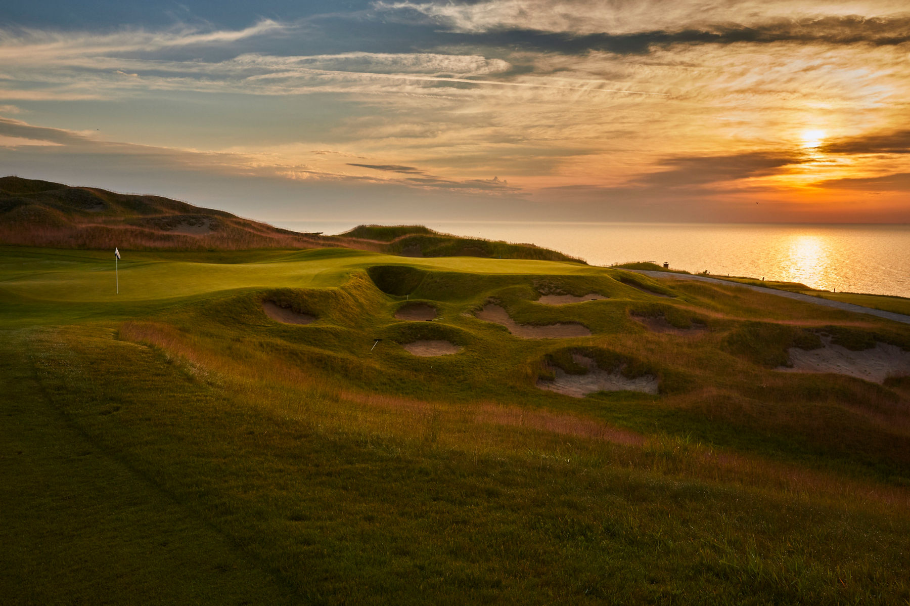 Wide, sweeping image of the beautiful natural landscapes at the KOHLER golf courses at sunset along the lake.