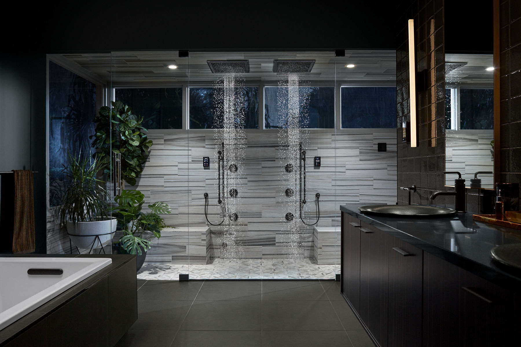 A large bathroom with a glassed-in shower area with striped light and dark gray floor and wall tile and matte black trim and accessories.