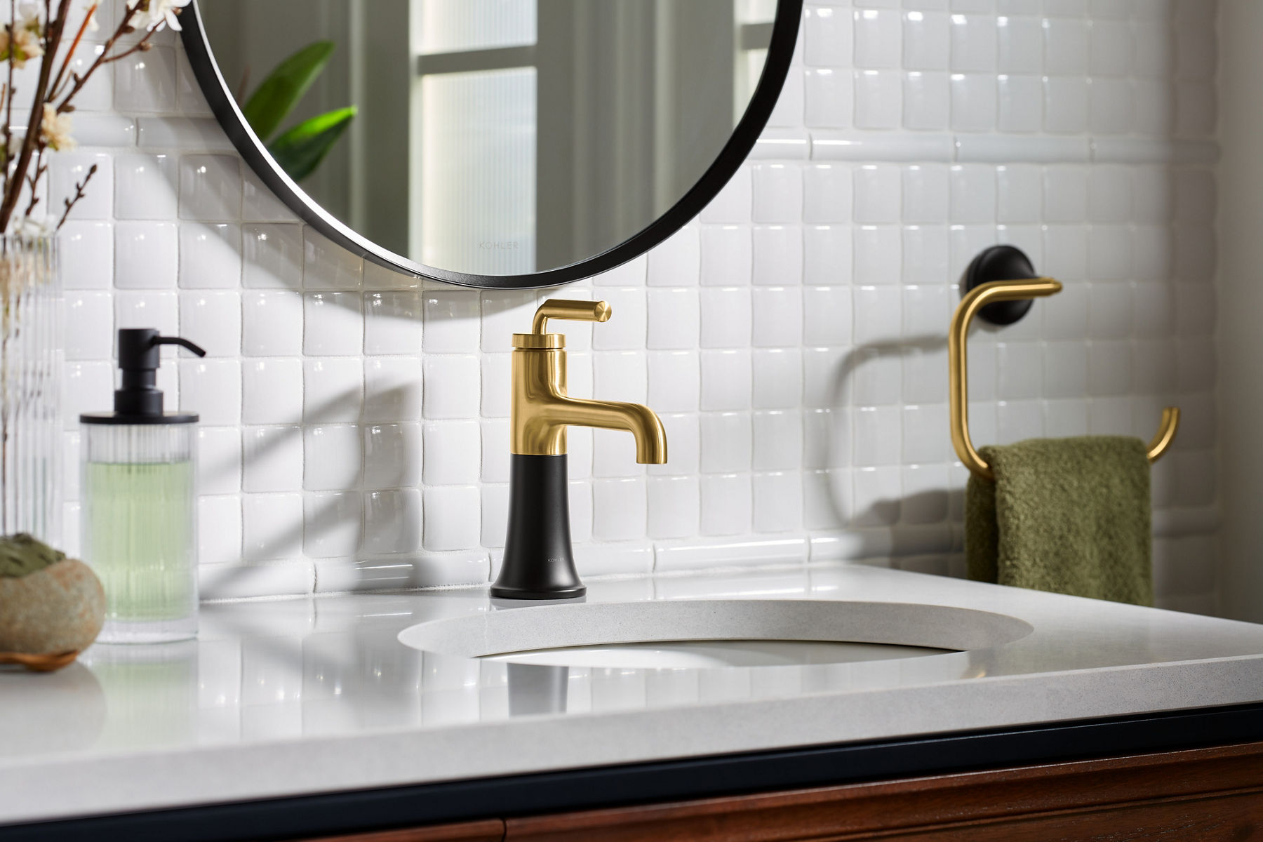 Un robinet à poignée à levier unique Tone de KOHLER en noir et or, installé sur un dessus de meuble-lavabo blanc.