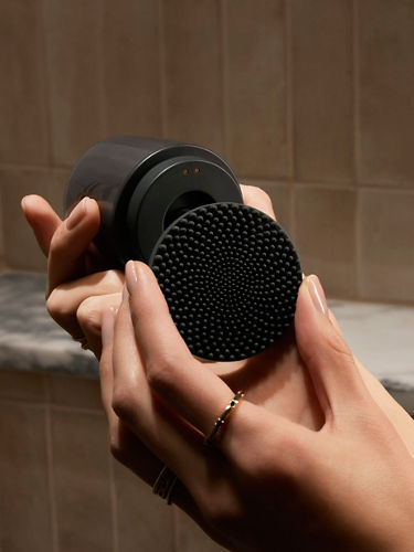 A close-up portrait product shot of a black-toned body scrubber that is opened