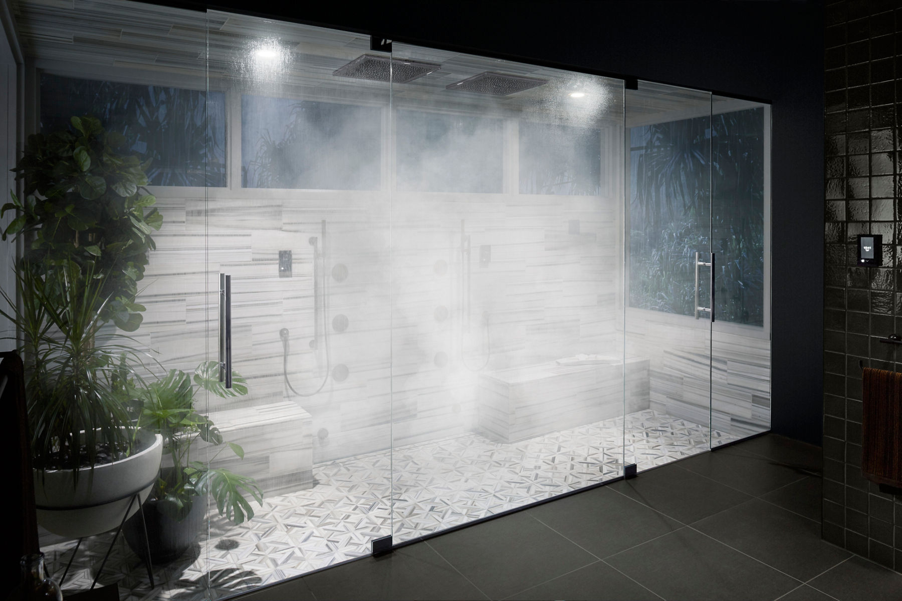 Portrait d’une salle de bain très embuée, fermée par des portes vitrées allant du plancher au plafond.