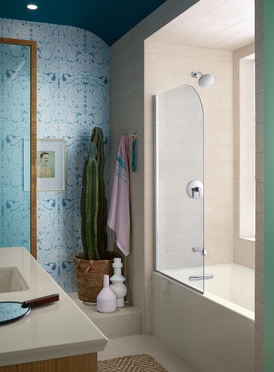 Écran de baignoire KOHLER avec baignoire en alcôve blanche aux murs beiges dans une salle de bain avec mur d’accent bleu clair et un cactus dans le coin.