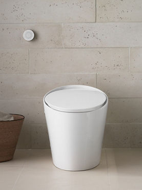 A white tankless toilet in a room with off white stone walls.