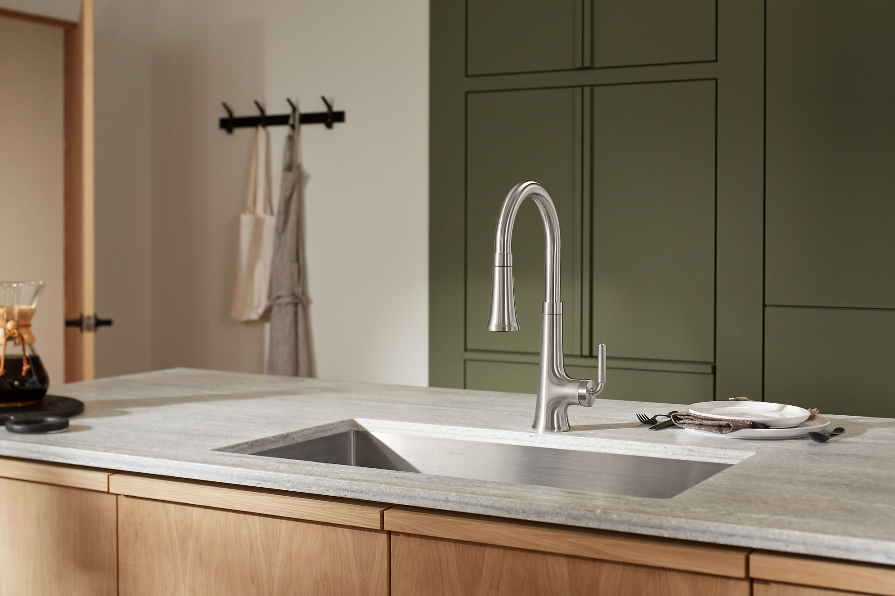 Un îlot de cuisine avec dessus blanc, évier en sous-surface et robinet rétractable à poignée à levier unique KOHLER.
