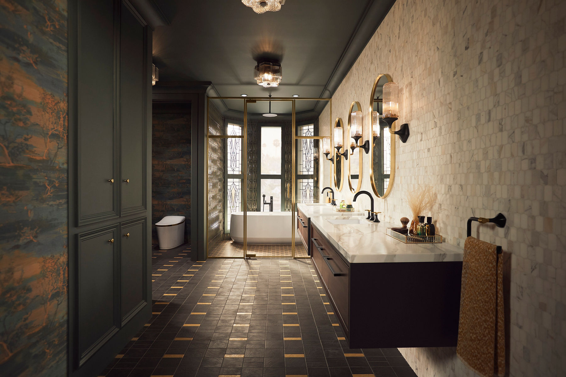 White tile, black and gold accents, and light marble add a touch of glamour to a bathroom with wall mounted vanities, a white KOHLER Ceric freestanding bath positioned in a bay window and a white Eir one-piece toilet in a separate alcove.