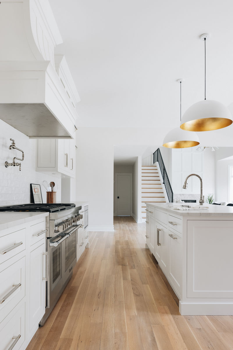 A white island with sink and KOHLER single hole faucet, in a white kitchen with large white range hood and pot filler faucet.