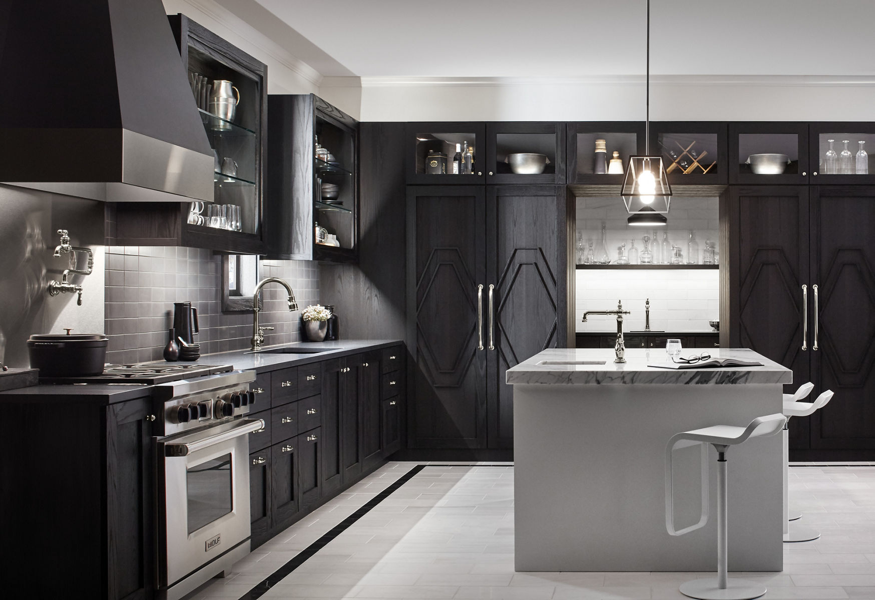 In a black and white kitchen with large island, modern cabinetry contrasts with the traditional lines of the KOHLER Artifacts pot filler, kitchen sink faucet, and bar sink faucet with Victorian spout design.