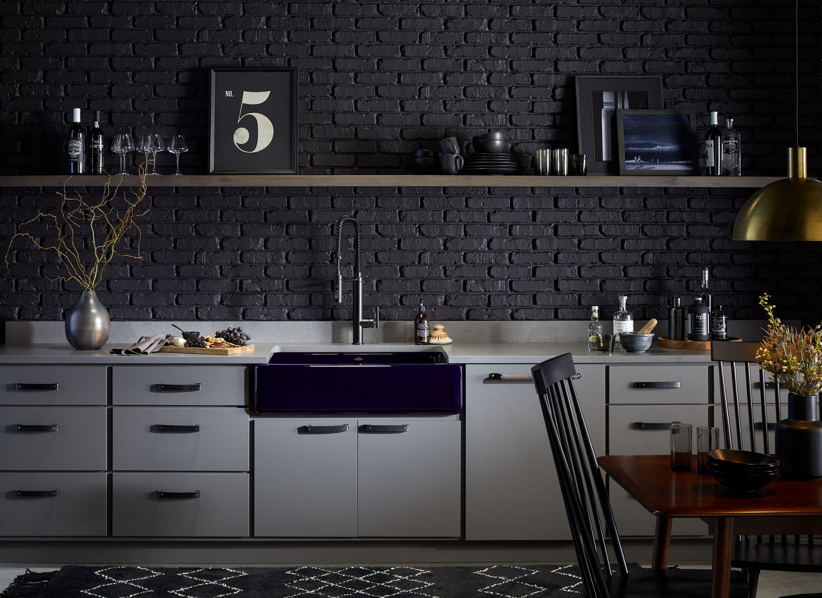 A kitchen with black brick wall, open shelving above white cabinets, KOHLER Whitehaven farmhouse sink in Indigo blue, and Purist Semi-professional kitchen sink.