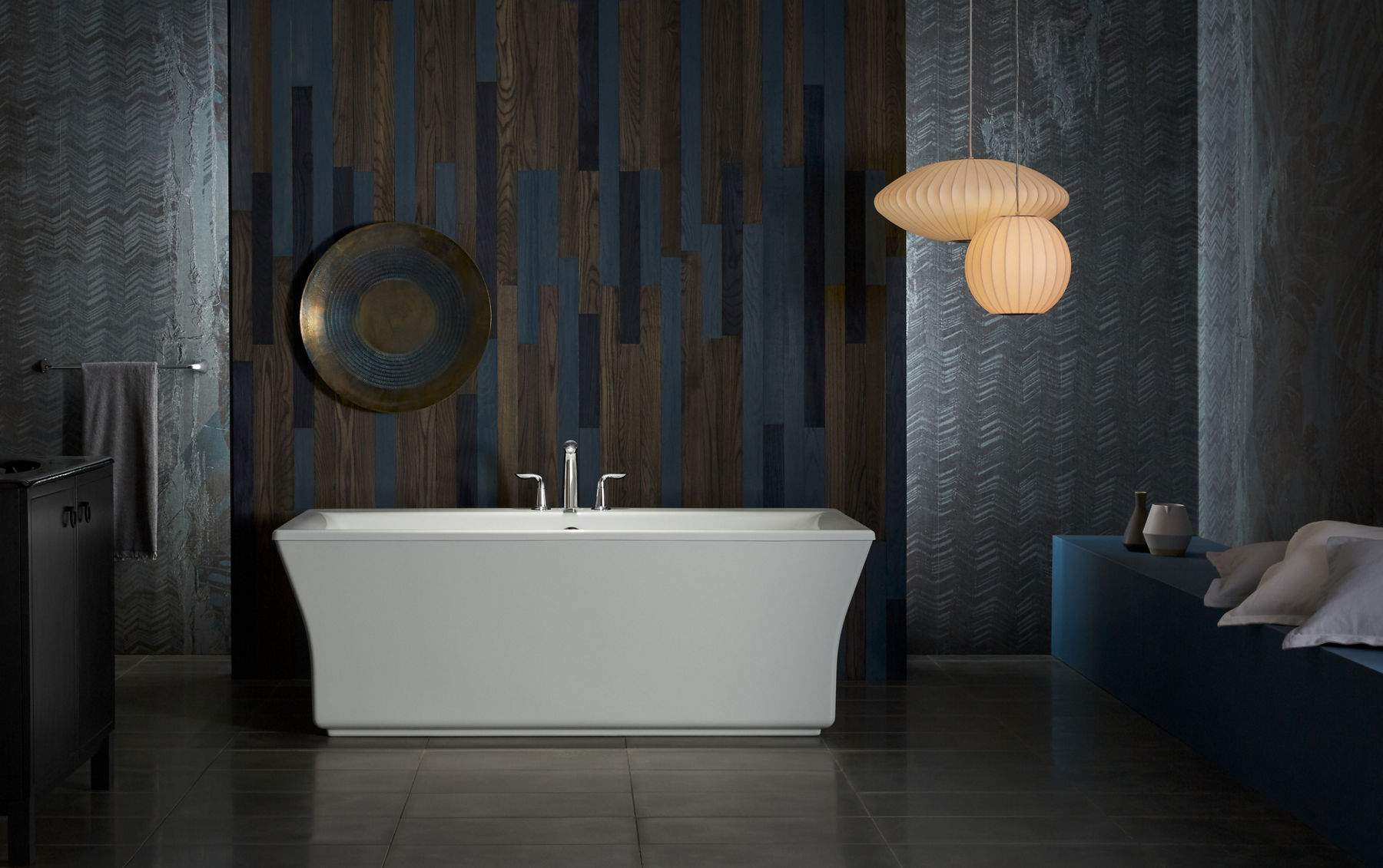 A white KOHLER Stargaze freestanding bath with Refinia bath trim makes a statement in a dark bathroom with vertical wood wall and two oblong white pendant lights.