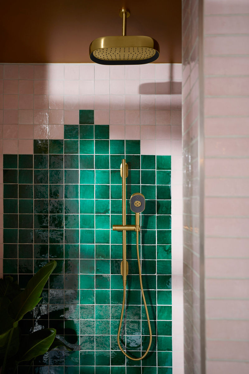 Image de la zone de douche dans la salle de bain conçue par Justina Blakeney pour la collection Heritage Color de Kohler. L’image met l’accent sur les accessoires de douche Statement au fini laiton, installés contre les murs de douche aux tuiles colorées.