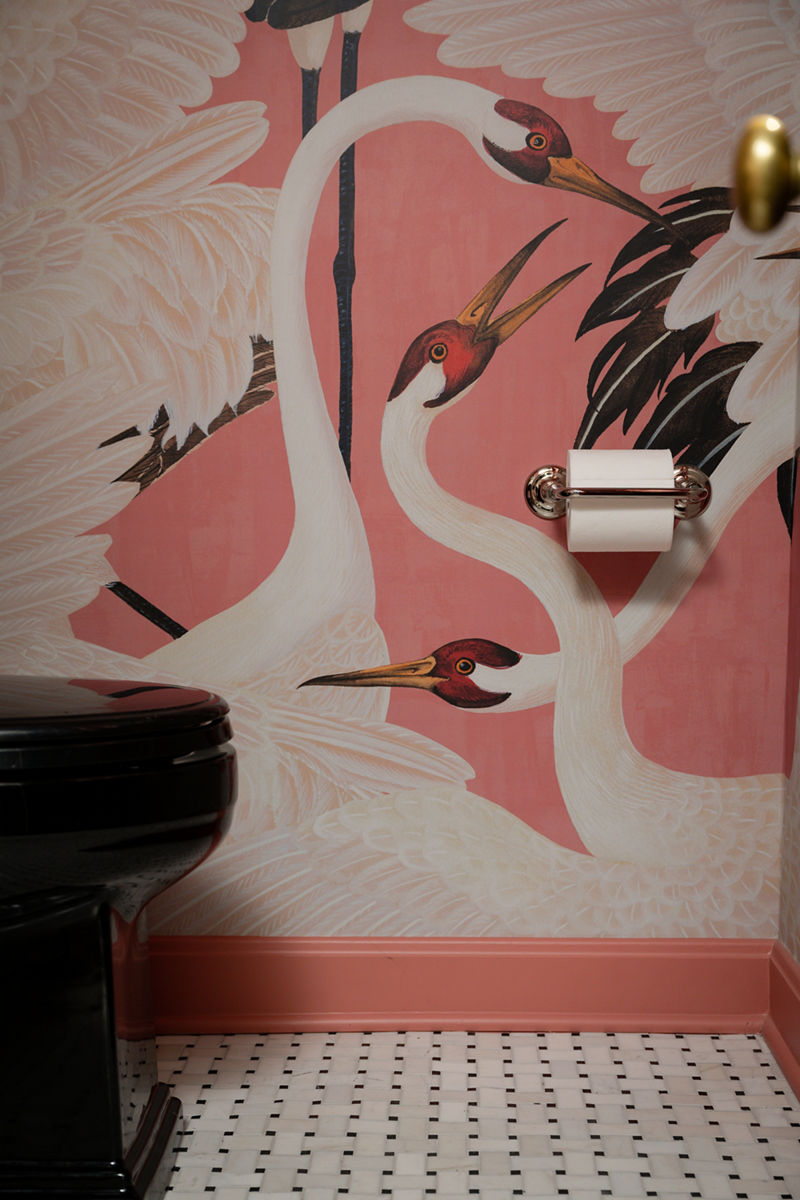 Gros plan d’un porte-papier hygiénique avec un rouleau de papier hygiénique, avec comme toile de fond un papier peint avec motif de cygne.