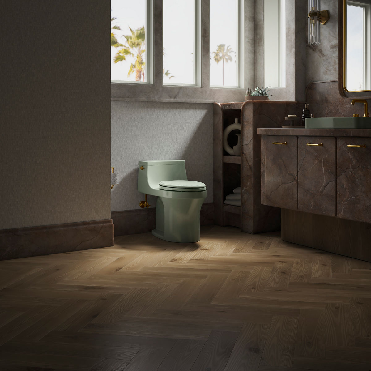 Image d’une toilette vert pâle dans une salle de bain avec robinetterie beige et brun rose et un plancher en chêne. Il y a du papier hygiénique à gauche et une tablette décorative à droite de la toilette.